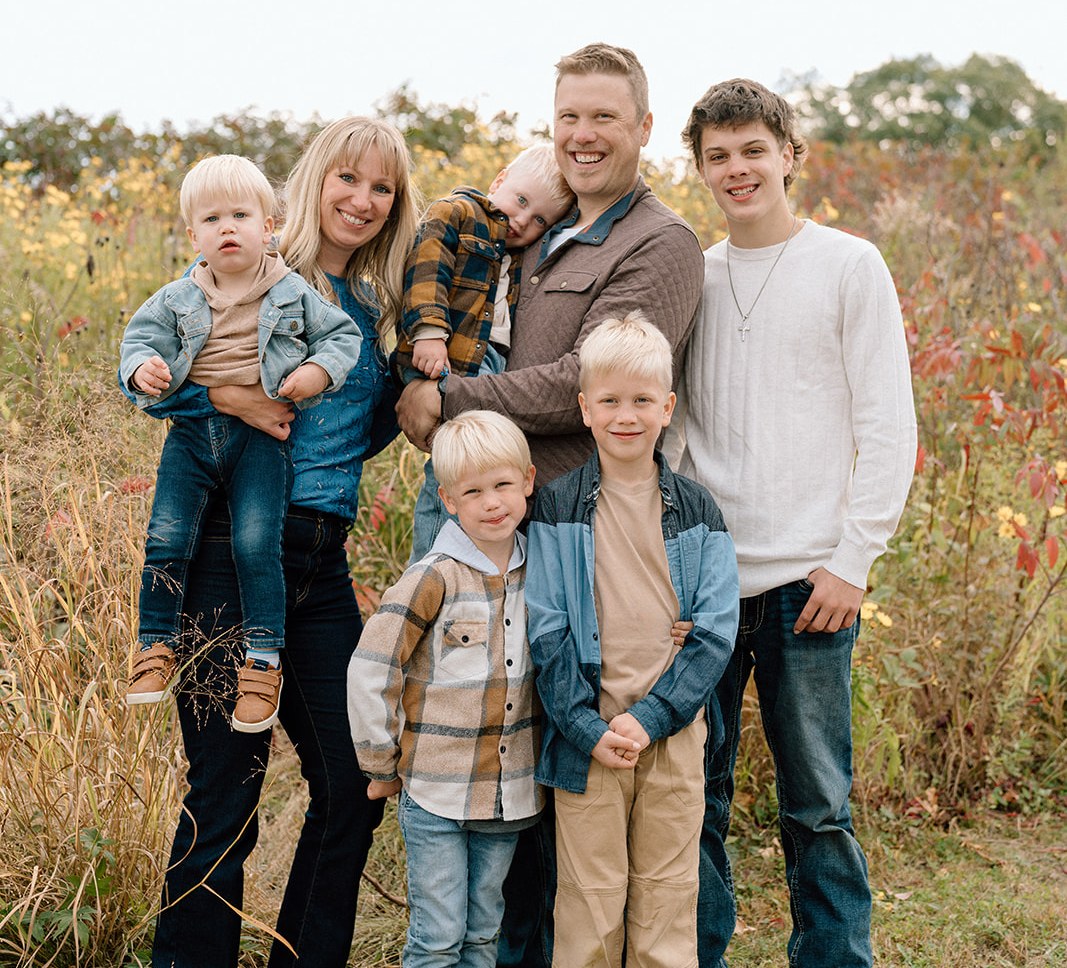 A family of seven smiling together in a field of fall wildflowers